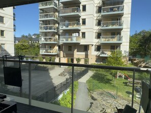 Een meerlaags woongebouw met balkons, een verhard gebied met banken en een speelplaats met een glijbaan.