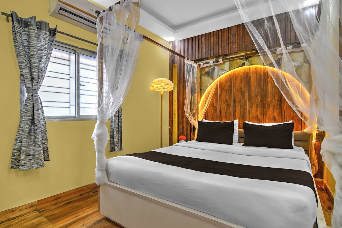 A bedroom with a bed, curtains, a nightstand, and a wall-mounted lamp.