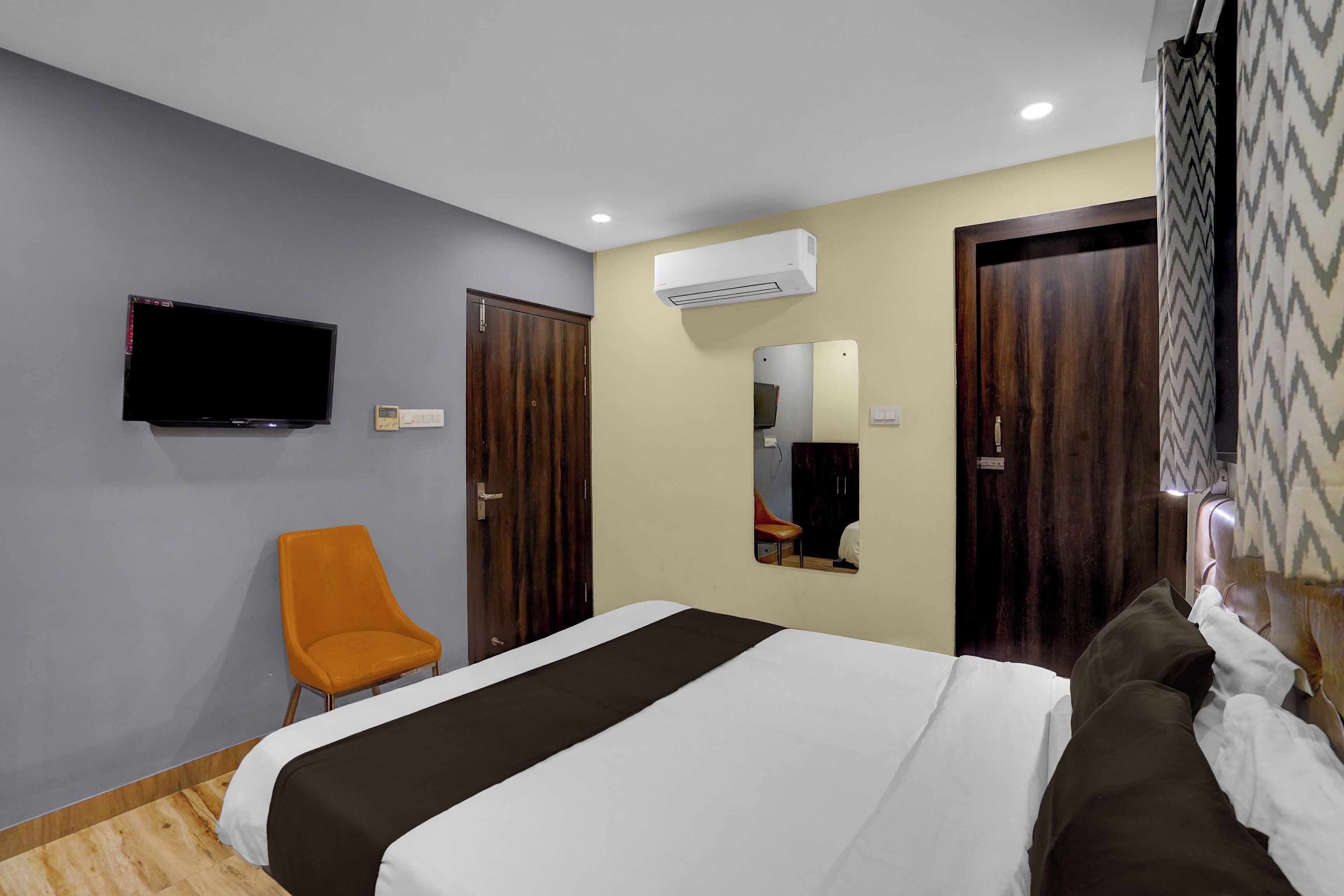 A hotel room with a bed, a television, an air conditioning unit, and a chair.