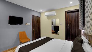 A hotel room with a bed, a television, an air conditioning unit, and a chair.