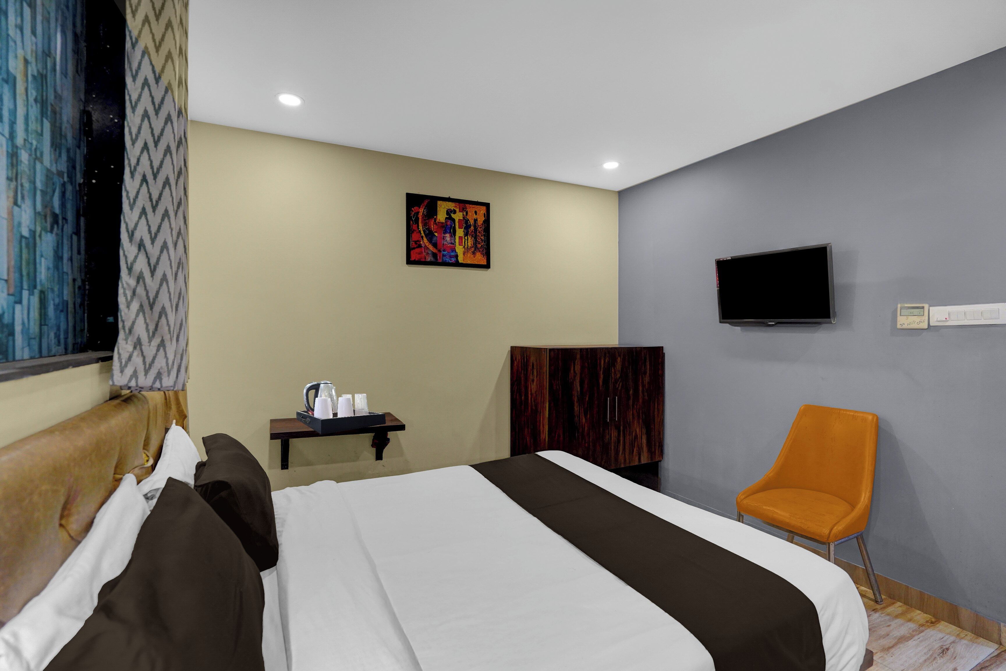 Una habitación de hotel con cama, televisión, silla, escritorio con tetera y un cuadro en la pared.