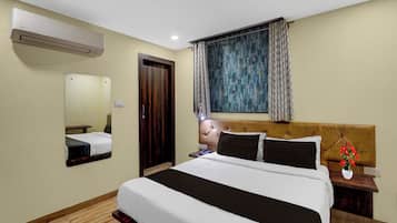 A hotel room with a bed, bedside table, lamp, and a window with curtains.