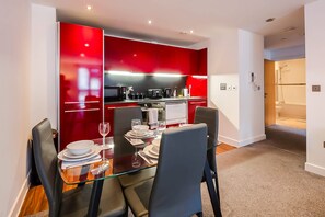 Un'area pranzo moderna con tavolo in vetro, pensili cucina rossi e un bagno adiacente.