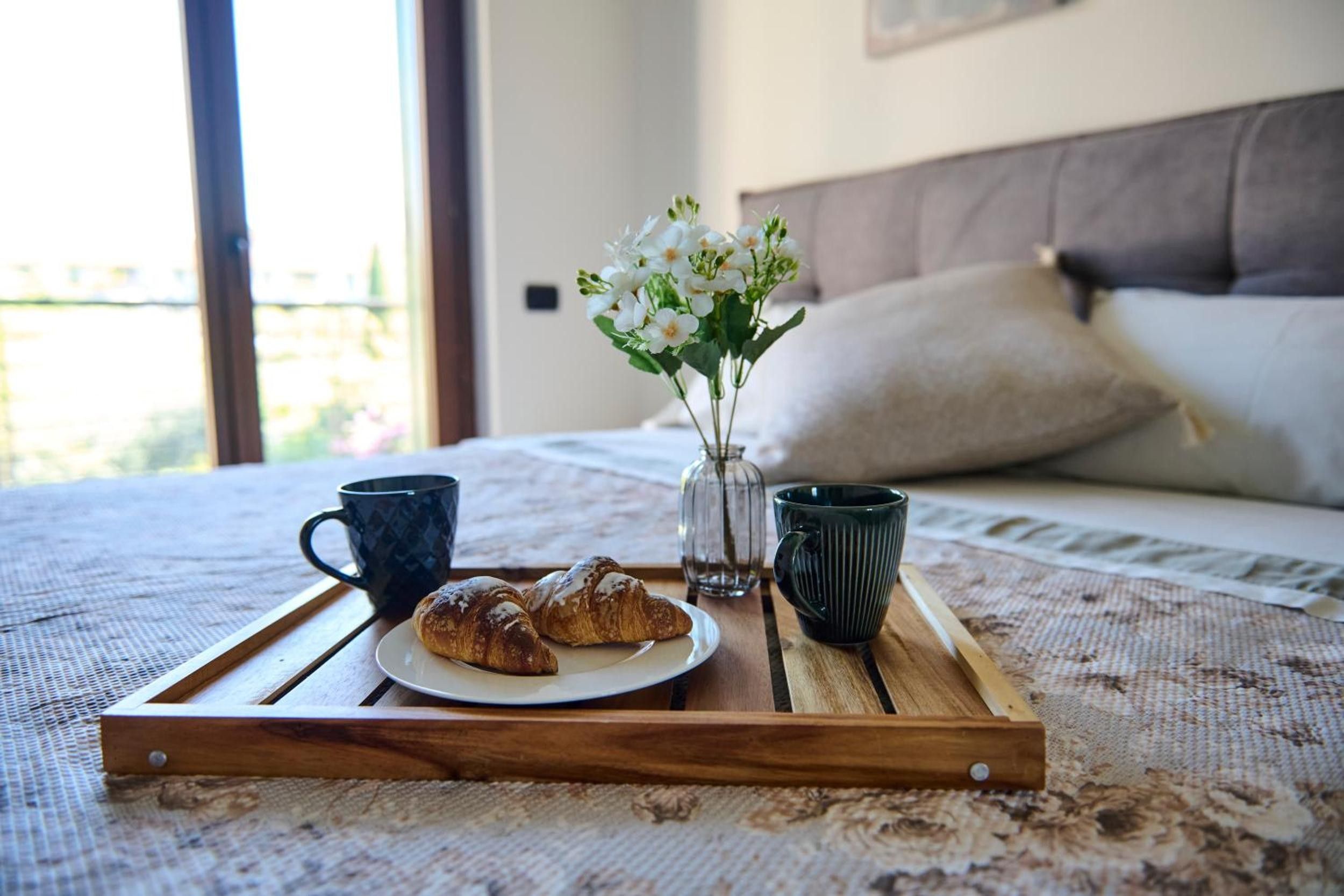 Ein hölzerner Tablett mit Croissants und zwei Tassen auf einem Bett mit floraler Bettdecke.