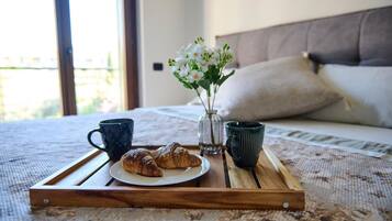 Ein hölzerner Tablett mit Croissants und zwei Tassen auf einem Bett mit floraler Bettdecke.