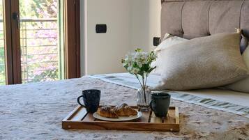Un letto rifatto con cura, un vassoio con croissant, un vaso di fiori e due tazze su un copriletto testurizzato.