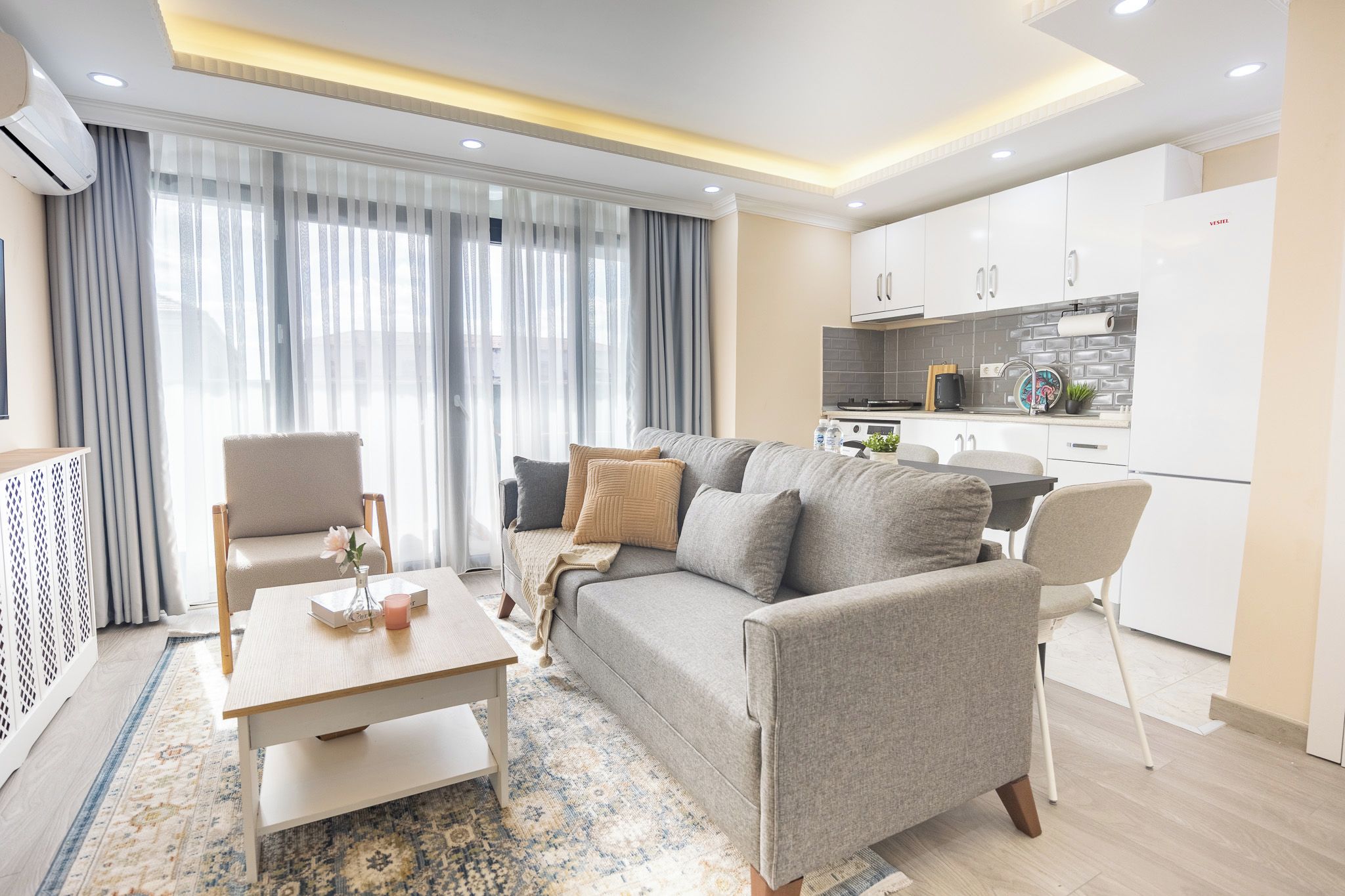 A modern living room with a sofa, chairs, a coffee table, and a kitchen area with cabinets and appliances.