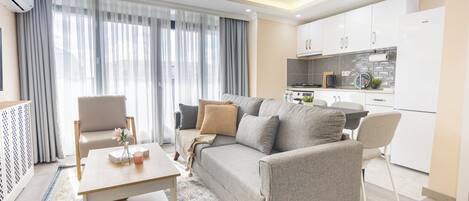 A modern living room with a sofa, chairs, a coffee table, and a kitchen area with cabinets and appliances.