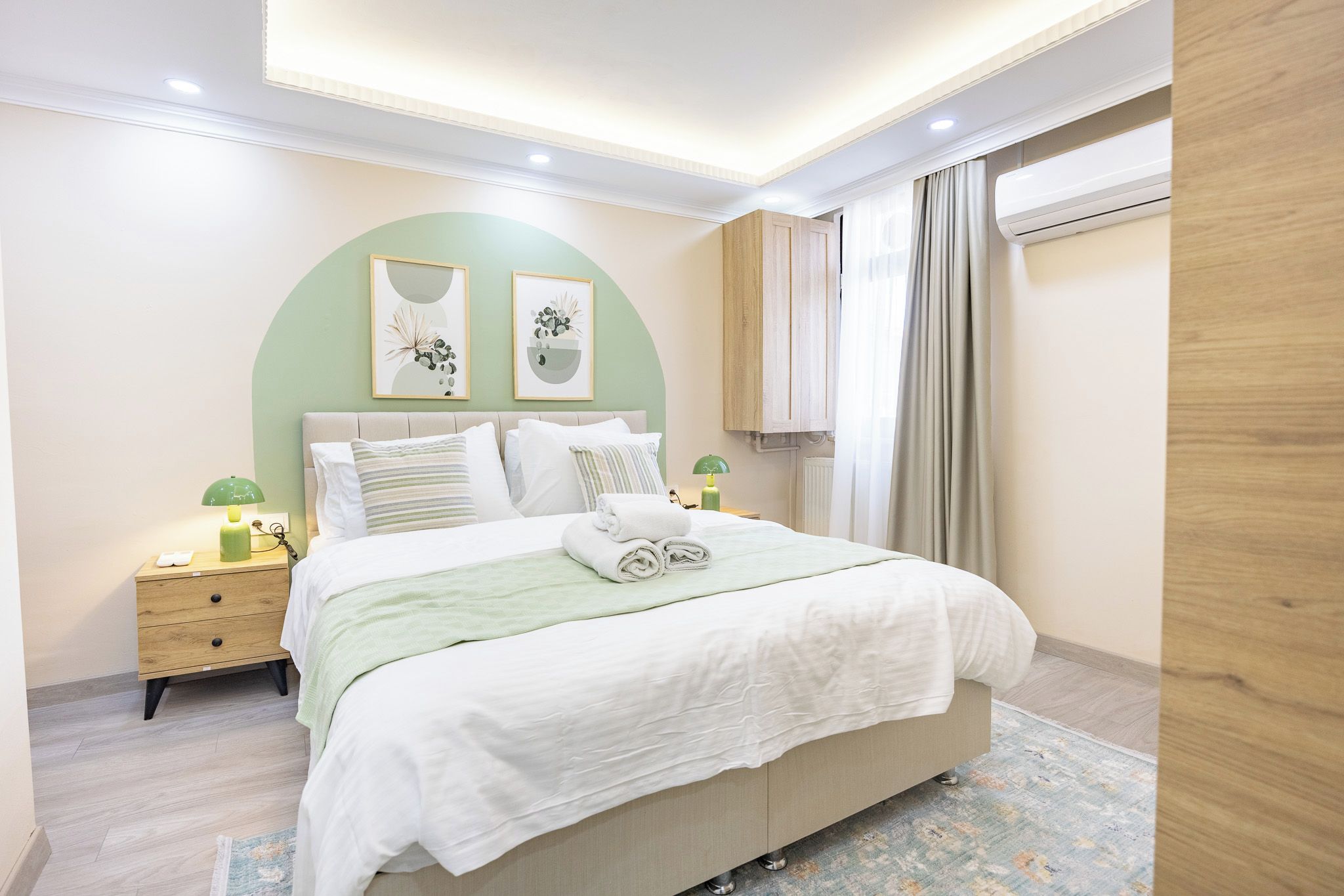 A bedroom with a bed, nightstands, a lamp, a window with curtains, and artwork on the wall.