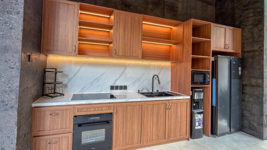 Una cocina moderna con armarios de madera, un lavamanos de acero inoxidable, microondas empotrado y un refrigerador negro.