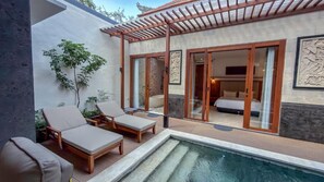 Zona junto a la piscina con sillones de descanso, una piscina pequeña y una habitación visible a través de puertas de vidrio.