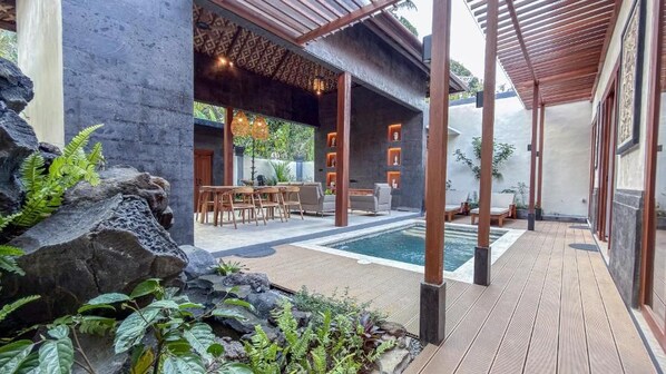 A wooden deck with a pool, outdoor seating, and a covered area with hanging lights.
