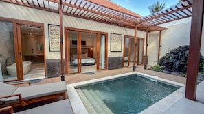 A modern outdoor pool area with a covered seating area and a bedroom visible through glass doors.