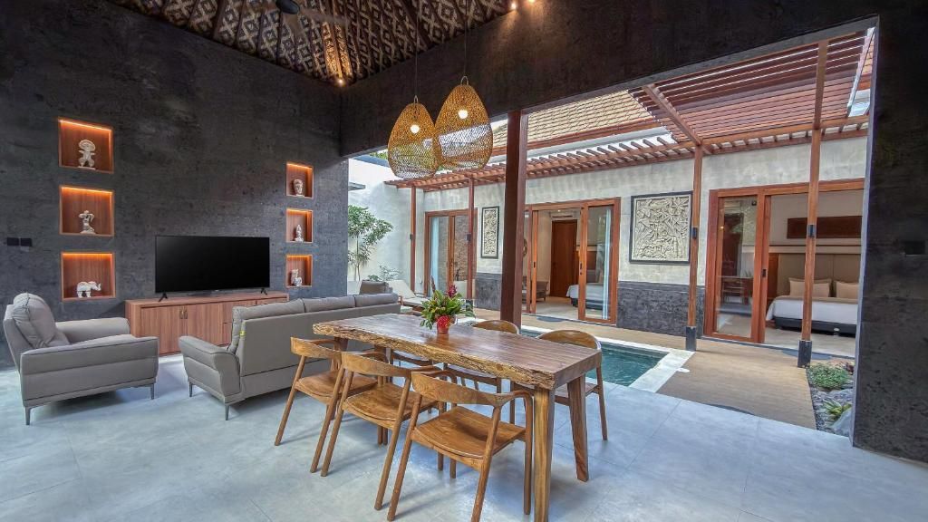 A modern living room with a flat-screen TV, a sofa, a dining table with chairs, and a pool area visible through the glass doors.