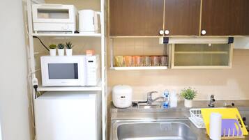 A compact kitchen with a microwave, toaster, and a small refrigerator. There is a sink with a faucet and a dish rack.