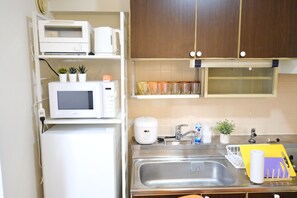 A compact kitchen with a microwave, toaster, and a small refrigerator. There is a sink with a faucet and a dish rack. - New Listing (板橋区)