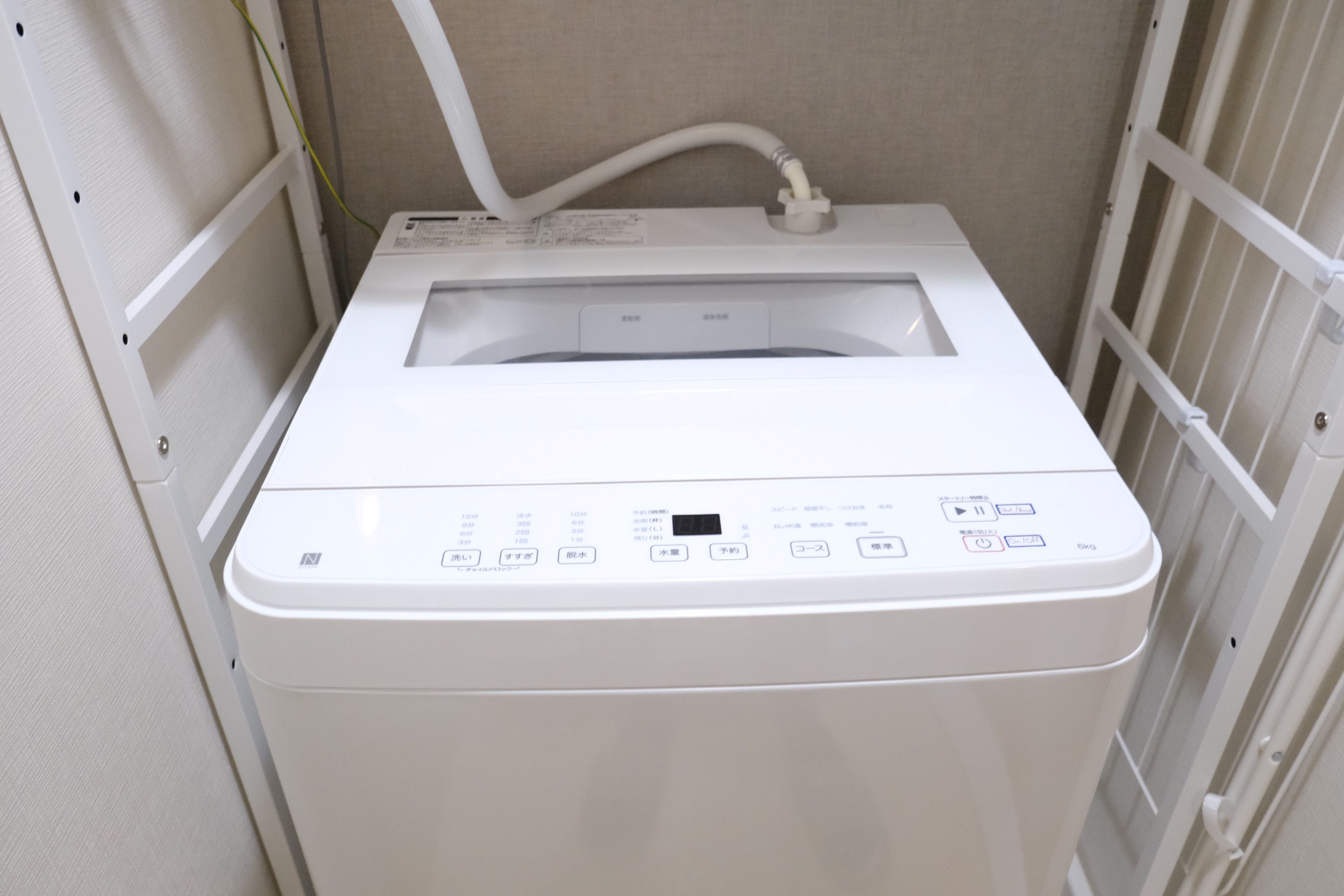 A white laundry machine with a control panel and a water inlet hose.