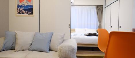 A hotel room with a bed, a sofa, and a chair. There is a poster on the wall.