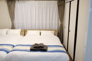 A hotel room with a large bed, two pillows, a folded towel, and a wardrobe. - New Listing (板橋区)
