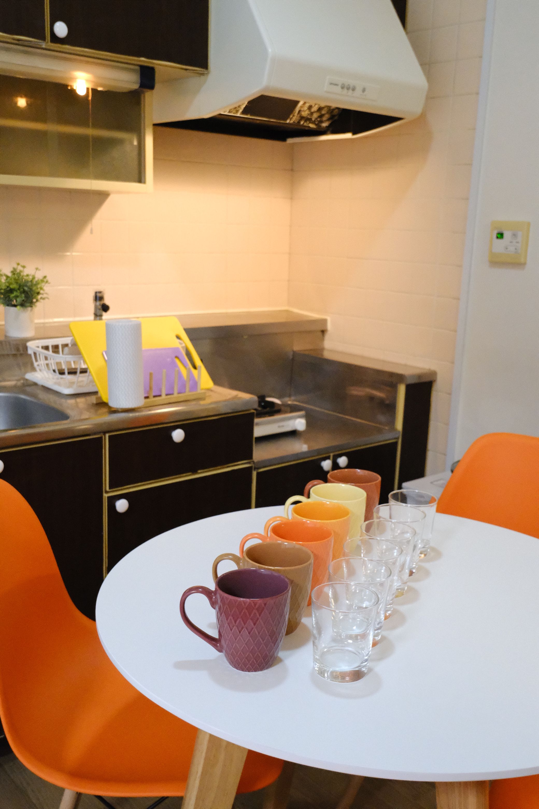 A kitchen with a white table set for dining, orange chairs, and a variety of mugs and glasses.