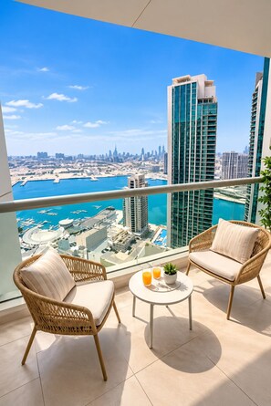 A balcony with wicker chairs and a small table, overlooking a cityscape with tall buildings and a marina. - 1BR Apartment - Stunning Sea Views - Pool & Gym - Al Reem Island (Abu Dhabi)