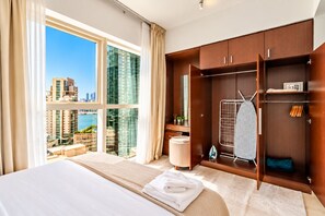 A hotel room with a large bed, a view of the cityscape, a wardrobe with hanging space, and a small seating area. - 1BR Apartment - Stunning Sea Views - Pool & Gym - Al Reem Island (Abu Dhabi)