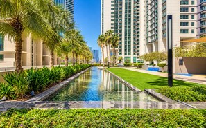 A modern urban setting with a reflective pool, palm trees, and high-rise buildings. - 1BR Apartment - Stunning Sea Views - Pool & Gym - Al Reem Island (Abu Dhabi)