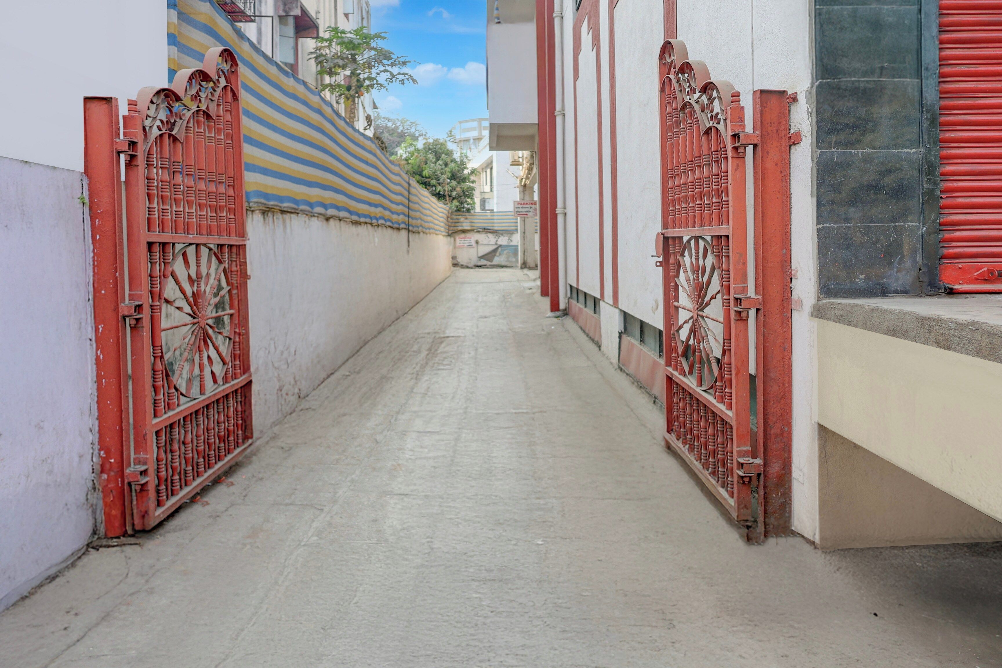 A narrow alleyway with red metal gates on both sides, leading to a building with a striped awning.
