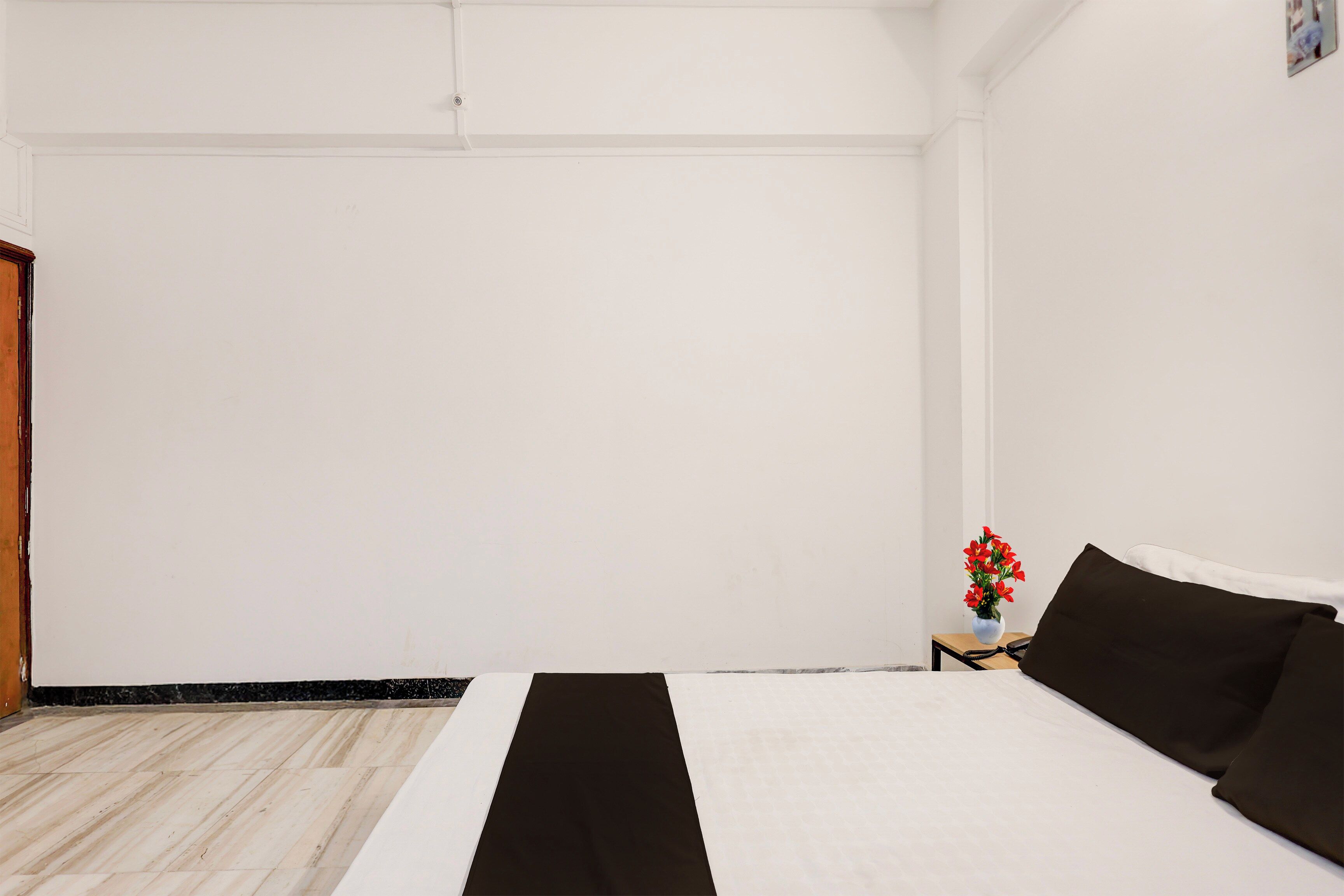 A hotel room with a bed, a small table with a vase of flowers, and a wooden door.