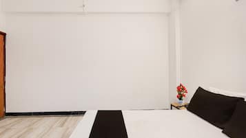 A hotel room with a bed, a small table with a vase of flowers, and a wooden door.