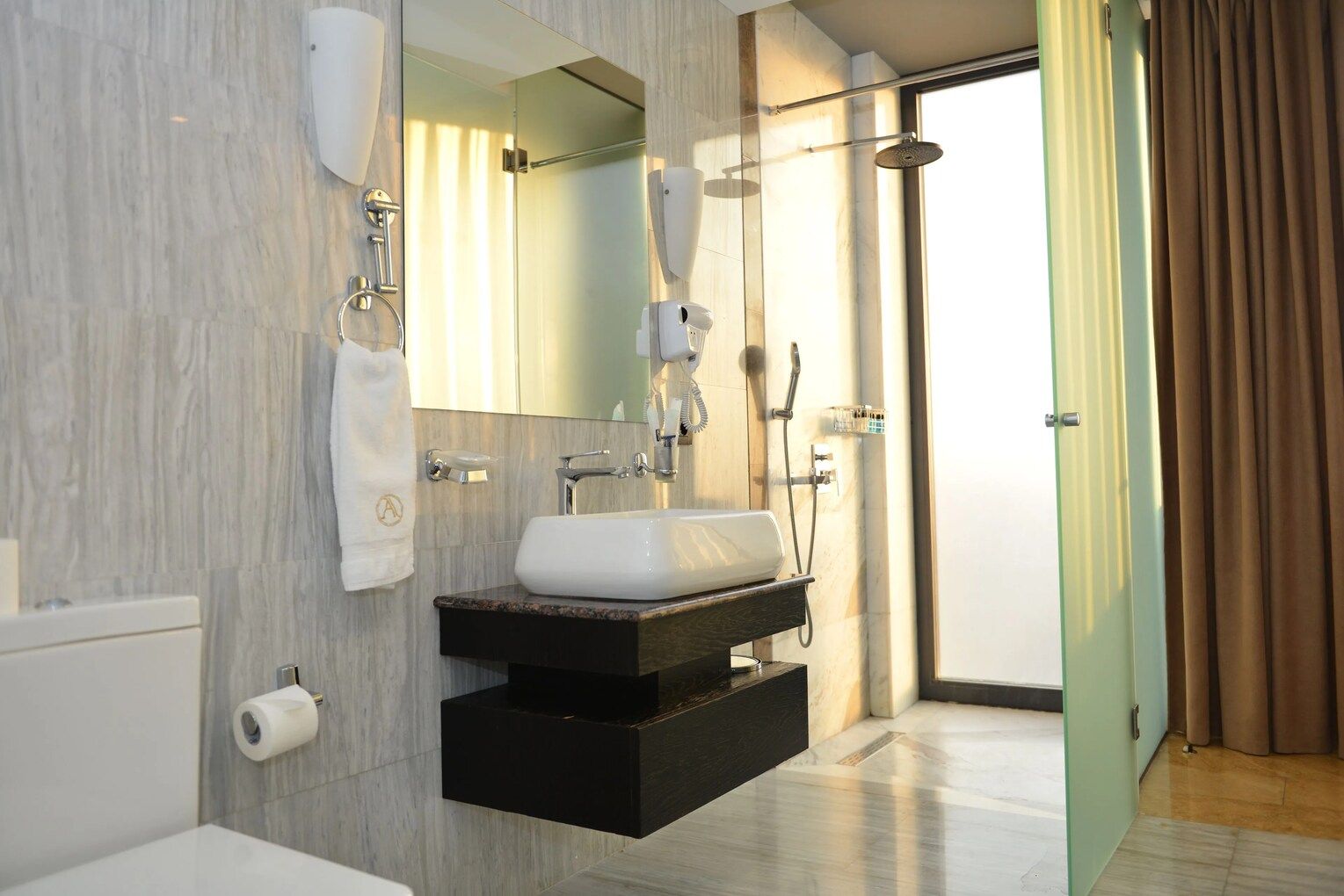 Un baño moderno con un lavamanos blanco, un espejo, un perchero para toallas y una zona de ducha.
