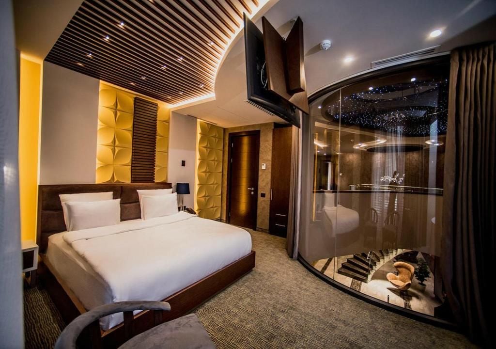 Une chambre d’hôtel moderne avec un grand lit, une cloison en verre et une vue sur un escalier.