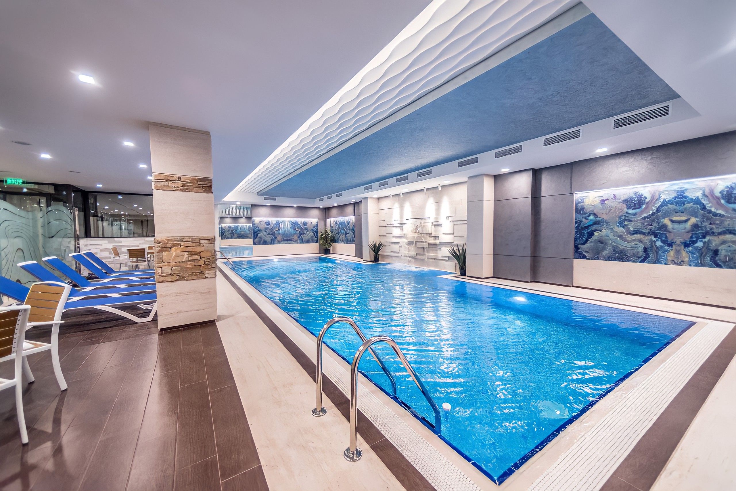 Une piscine intérieure dotée de chaises longues et d’un mur décoratif en pierre.