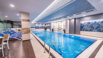 Une piscine intérieure dotée de chaises longues et d’un mur décoratif en pierre.