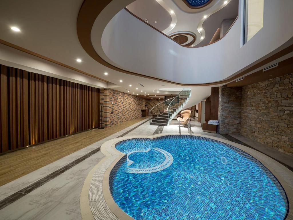 Una piscina interior moderna con diseño circular, una escalera y una pared de madera.