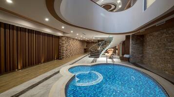 Una piscina interior moderna con diseño circular, una escalera y una pared de madera.