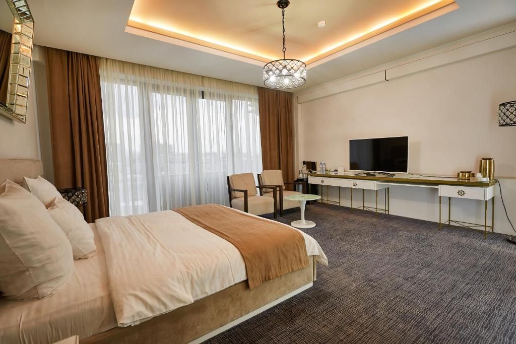 A hotel room with a bed, a desk with a television, a chair, and a small table.
