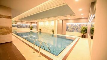 A modern indoor swimming pool with clear water, surrounded by walls with textured patterns and potted plants.