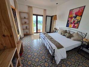 Un dormitorio con una cama, un armario de madera, una estantería con adornos y un suelo colorido.
