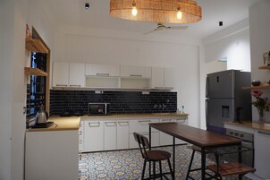 Una cocina moderna con gabinetes blancos, un salpicadero de baldosas negras, una mesa de comedor de madera con dos sillas y un refrigerador de acero inoxidable.