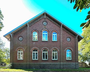 A red brick building with multiple arched windows and a central circular window. - Apartment in a Historic Hallenhaus on Butjadingen (Butjadingen)