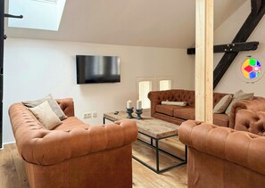 A modern living room with leather sofas, a wooden coffee table, a flat-screen TV, and a staircase with a wooden railing. - Apartment in a Historic Hallenhaus on Butjadingen (Butjadingen)