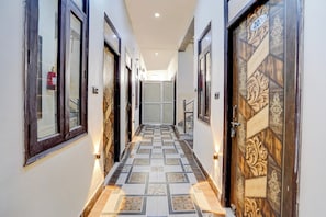 A hallway with patterned flooring, doors with decorative designs, and a light fixture on the wall. - Hotel O Prem Mandir (Mathura)