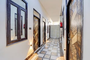 A hallway with patterned tiled flooring, wooden doors with decorative designs, and a fire extinguisher mounted on the wall. - Hotel O Prem Mandir (Mathura)