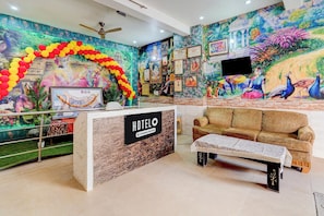 A hotel reception area with a reception desk, a sofa, and a mural with peacocks. - Hotel O Prem Mandir (Mathura)