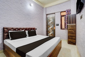 Une chambre à coucher comprenant un lit, une tête de lit en bois, un téléviseur fixé au mur et une porte ornée de panneaux décoratifs.