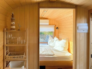 A wooden interior with a bed, a shelf with glassware, and a window. - Tiny House with a view by the Wadden Sea (Butjadingen)