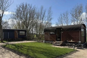 A small, rustic cabin with a wooden exterior, a front porch with seating, and a clear sky in the background. - Tiny House with a view by the Wadden Sea (Butjadingen)