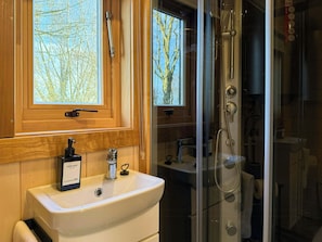 Ein Badezimmer mit einem Holzbadezimmermöbel, einem Handseifenspender, einem Waschbecken und einer Duschkabine aus Glas.