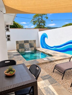 A swimming pool with a wave mural, a table with a plant, and outdoor seating. - Blue Wave House I Ocean Villas (Playas Del Coco)